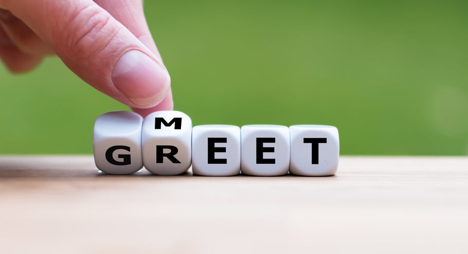 Hand is turning a dice and changes the word 'Meet' to 'Greet'